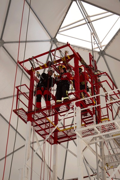 Alumnos con arnés y casco trabajando sobre una plataforma metálica roja de entrenamiento en altura dentro del domo de Macaya Safety